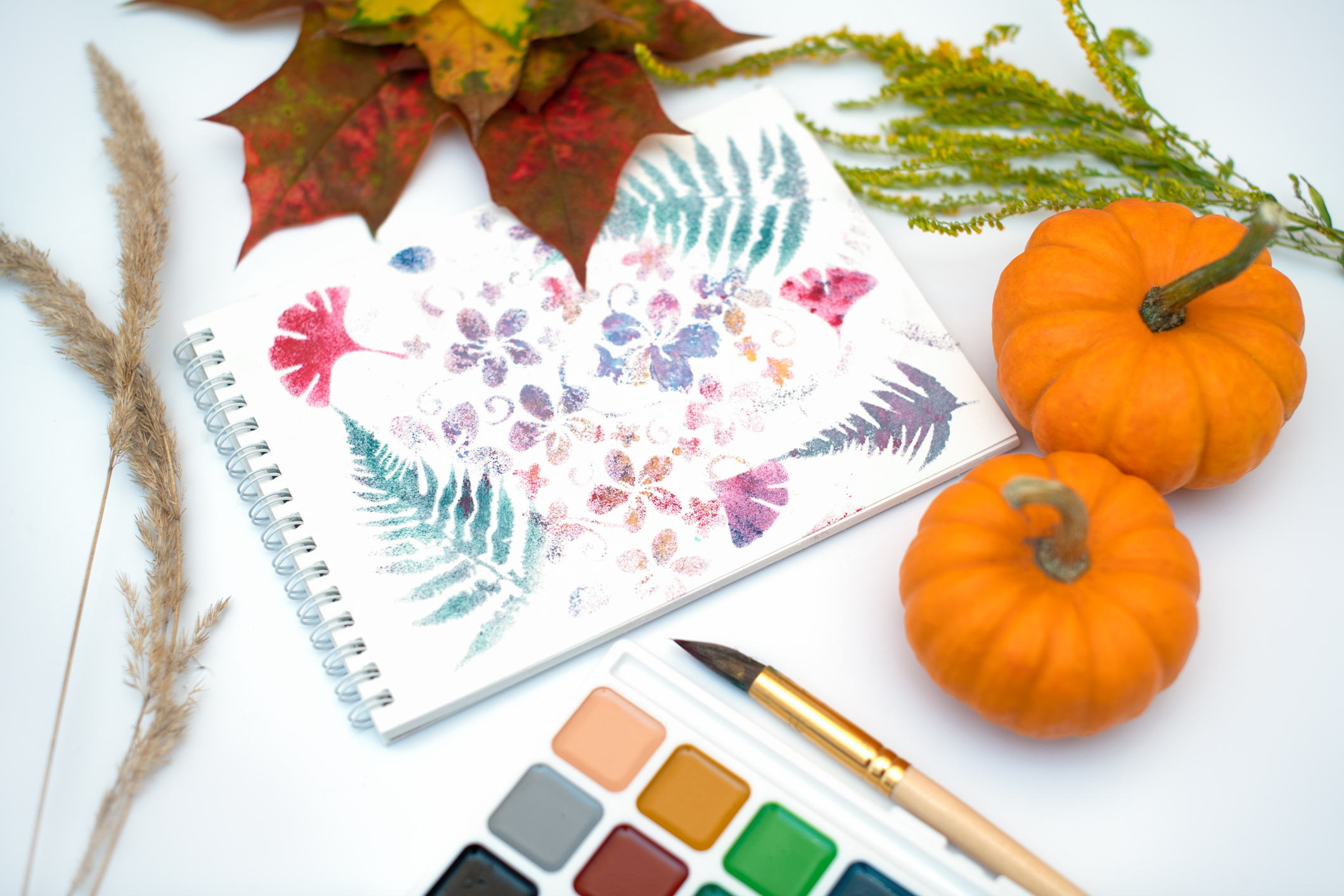 Workplace of artist. Sheet of paper, Set of watercolor paints, brush and autumn leaves. Autumn concept. Top view.